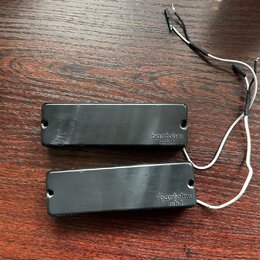Dvě černé elektrické kytarové snímače typu humbucker s připojenými bílými vodiči. Na obou snímačích je vpravo nápis bartolini mh 1. Povrch plastových…