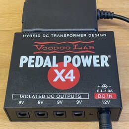 Černý napájecí adaptér s nápisy HYBRID DC TRANSFORMER DESIGN, Voodoo Lab a PEDAL POWER X4. Spodní část obsahuje čtyři výstupy označené jako ISOLATED…