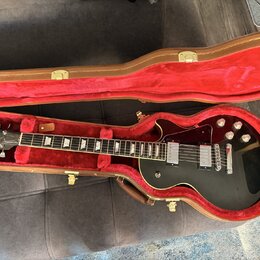 Černá elektrická kytara s tvarem single-cut v hnědém kufru s červeným vnitřkem. Na hlavě je bílé logo Gibson, na hradle jsou dva humbuckery a čtyři o…