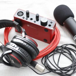 Sada červeného a černého audio vybavení na světlém podkladu. Obsahuje červený zvukový interface s nápisem Focusrite, černý mikrofon s popsem a nápise…