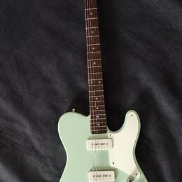 Světle zelená elektrická kytara s bílým pickguardem a hnědým hmatníkem. Na hlavě je viditelné logo Squier. Kytara má dva snímače a tři ovládací knofl…