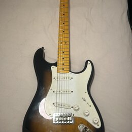 Elektrická kytara s tónem těla v provedení sunburst a bílým pickguardem. Na hlavě hředu je viditelné logo Fender. Nástroj má javorový hmatník a tři s…