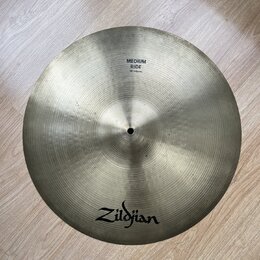 Kruhový činely v zlatavé barvě s viditelným koncentrickým broušením povrchu. Na činely jsou černé nápisy Zildjian a MEDIUM RIDE 18"/46cm. Povrch vyka…