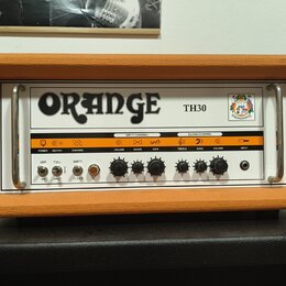 Kytarový zesilovač v oranžovém vinylu s bílým předním panelem. Na panelu je velký nápis ORANGE a označení modelu TH30 spolu s logem. Zesilovač obsahu…