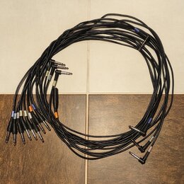 Sada černých audio kabelů s 6,3mm jack konektory. Některé konektory mají barevné značky v modré, oranžové a bílé barvě. Kabely jsou svinuté do kruhu…