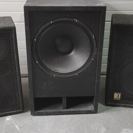 Tři černé reproduktorové bedny s povrchem z hrubého materiálu. Prostřední bedna obsahuje jeden velký basový reproduktor a v dolní části má otevřený p…