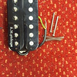 Černý humbucker s dvěma řadami šesti bílých pólů. Na levé straně je nápis R.M.pickups. K snímači vedou elektrické vodiče a vedle něj jsou položeny dv…