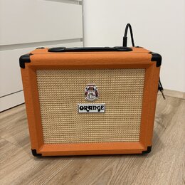 Kytarový kombo zesilovač s oranžovým texturovaným povrchem a béžovou přední síťovkou. Na mřížce je umístěno logo ORANGE a nad ním kulatý štítek s neč…