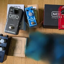 Fotografie zobrazuje čtyři kytarové efekty s jejich krabicemi na dřevěné podlaze. Jsou zde pedály: černý tc electronic DITTO STEREO LOOPER, modrý ANG…