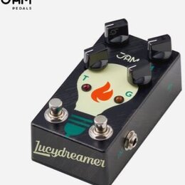 Černý kytarový efekt s nápisem Lucydreamer na spodní hraně a logem JAM v horní části. Na povrchu je grafika žluté žárovky s oranžovým plamenem uvnitř…