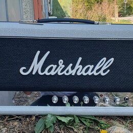 Kytarový kombo zesilovač v šedém vinylovém potahu s černou mřížkou, na které je bílý nápis Marshall. Spodní ovládací panel obsahuje červený vypínač,…