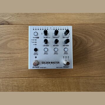 Stříbrný efektový pedál s nápisem GOLDEN MASTER PEDAL a doplňkovým textem 24 BIT 96 KHZ. Zařízení má několik otočných potenciometrů s popisky VU IN O…