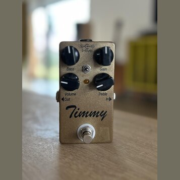 Kytarový efekt pedál v bronzové barvě s kovovým povrchem. Na přední straně jsou čtyři černé otočné knoflíky s popisky Bass, Gain, Volume a Treble. Up…