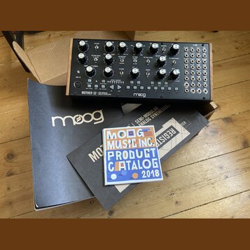 Semi-modulární analogový syntetizátor v dřevěném šasi s černým ovládacím panelem. Na přední straně je nápis MOTHER-32 SEMI-MODULAR ANALOG SYNTHESIZER…