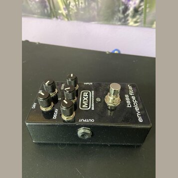 Černý efekt pedál s nápisy MXR, BASSINNOVATIONS a bass envelope filter. Na horní straně jsou čtyři ovládací knoflíky s popisky DRY, FX, SENS. a DECAY…
