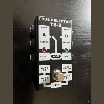 Černý efektový pedál s bílými nápisy TRUE SELECTOR a TS-2. Na horní části jsou označení SEND, RETURN, A, B, OUTPUT a INPUT s logem AMIT v oválu, dopl…