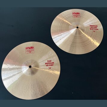 Dvě stříbrné činely z mosazi s viditelným broušením povrchu. Na levém číneli je červený nápis PAISTE 2002 MADE IN SWITZERLAND a text TOP MEDIUM HI-HA…