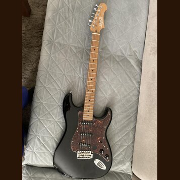 Černá elektrická kytara s hnědým hnedým hmatníkem a tmavě hnědým vzorovaným pickguardem. Na hlavě je viditelné logo "Squier". Kytara má tři snímače,…