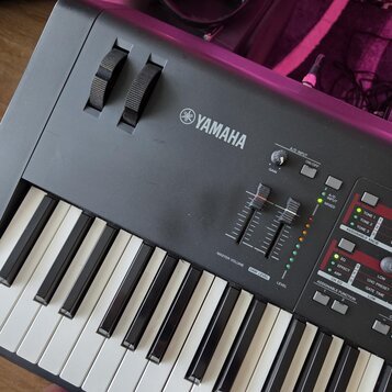 Detailní pohled na ovládací panel a klávesy černého digitálního klavíru značky YAMAHA. Na panelu jsou vidět posuvníky s popisky MASTER VOLUME, DAW LE…