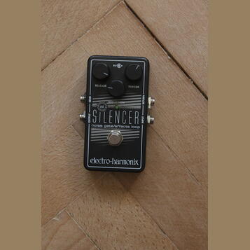Černý efekt pedál s nápisem THE SILENCER a doplňkem noise gate/effects loop. Na horní části jsou dva černé ovládací knoflíky s popisky RELEASE a THRE…