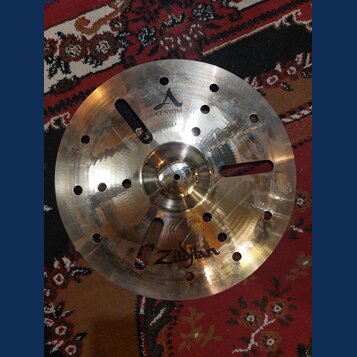 Kovový činel s vryty a otvory v povrchu. Na povrchu je nápis CUSTOM a logo Zildjian. Činely vykazují známky používání v podobě drobných škrábanců a z…