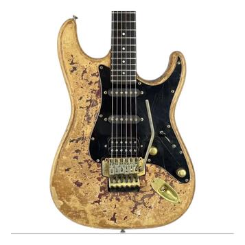 Elektrická kytara s tvarem typu Stratocaster v žluté barvě s výrazným efektem opotřebení a odloupaného laku. Nástroj má černý pickguard, tři snímače…