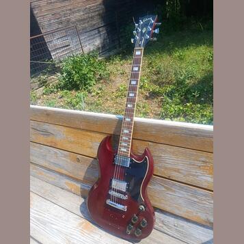 Tmavě červená elektrická kytara s černým pickguardem a hnedým hmatníkem. Na hlavě je zlatý nápis Gibson. Nástroj má dva humbuckery, čtyři ovládací kn…