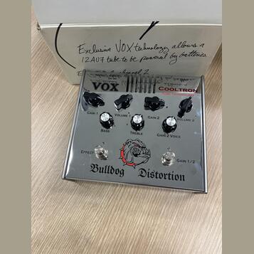 Stříbrný efekt pedál s nápisem Bulldog Distortion a logem hlavy buldoka. Na horním panelu je značka VOX a nápis COOLTRON TUBE TECHNOLOGY. Zařízení má…