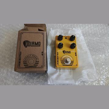 Žlutý efekt pedál s nápisy DOLARMO a OVERDRIVE. Na horní straně jsou dva černé oválné knoflíky s popisky BASS a TREB, dále nápisy GAIN a LEVEL. V dol…