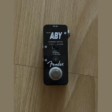 Černý kytarový pedál s nápisy MICRO ABY a Fender. Na horní části je vstup DC IN a přepínač CHANNEL SWITCH s označením A/B ● Y(A&B) a popisem A:RED, B…