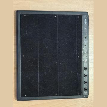 Černý obdélníkový pedálboard s povrchem z černého textilu. Na pravé straně je ovládací panel s nápisem Warwick a pod ním menším písmem BY WARWICK. Pa…