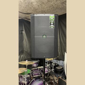 Černý reproduktor s mřížkou, umístěný na stojanu. V pravém horním rohu je zelený štítek s nápisy TRUMP SERIES, 1400W OF POWER, MUSIC DUCKING a FEEDBA…