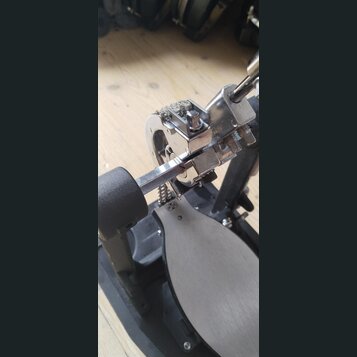Detailní pohled na kový mechanismus basového pedálu s černou základnou a šedým stupňem. Konstrukce je z chromovaného kovu s viditelnými šrouby a nast…