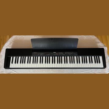 Černý digitální piano s klávesnicí. Na horním panelu a na krytu je bílý nápis YAMAHA. V pravé části ovládacího panelu je uveden model P-85. Povrch kr…