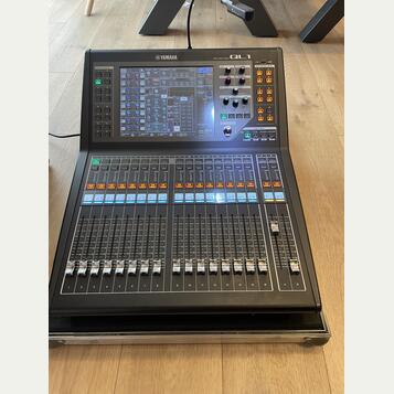 Černý digitální mixovací pult značky YAMAHA, model QL1. Horní část obsahuje barevný displej s ovládacími prvky, několik posuvníků a tlačítek. Spodní…