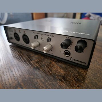 Stříbrno-černý zvukový interface značky steinberg. Na předním panelu jsou nápisy Rupert Neve Designs TRANSFORMER, NES a steinberg. Zařízení obsahuje…