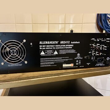 Zadní strana černého rackového zařízení s nápisem ALLEN&HEATH AR2412 AudioRack. Na šasi jsou umístěny varovné štítky s texty CAUTION, RISK OF ELECTRI…