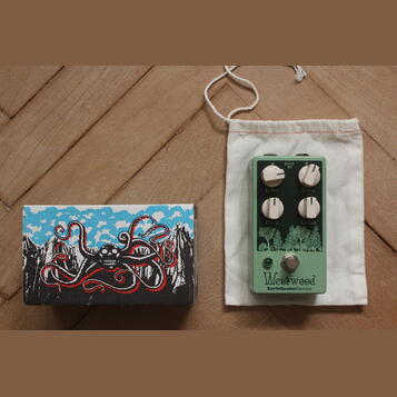 Zelený efekt pedál s nápisy Level, Drive, Bass a Treble u ovládacích knoflíků. Ve spodní části je logo Westwood a text EarthQuakerDevices. Vedle pedá…