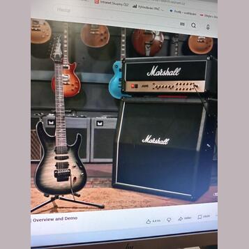 Fotografie zachycuje elektrickou kytaru s černým gradientem a dvě komba značky Marshall. Horní kombo má nápis Marshall a modelové označení JVM, spodn…