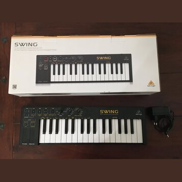 Černý MIDI kontrolér s klávesami, napájecí adaptér a originální kartonová krabice. Na přístroji je žlutý nápis SWING a pod ním text MIDI CONTROLLER S…