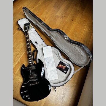 Černá elektrická kytara s typickým tvarem SG, equipped s dvěma humbuckery a čtyřmi ovládacími knoflíky. Na hlavě hmatníku je vidět nápis Gibson. Kyta…