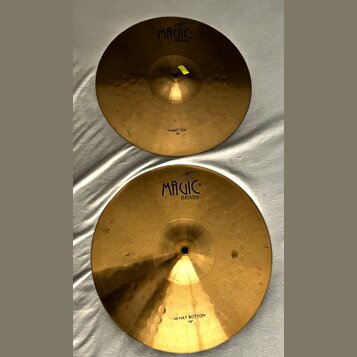 Dvě mosazné činely v zlatavé barvě. Oba mají nápis MAGIC BRASS a jsou označeny jako HI-HAT TOP 14" (horní) a HI-HAT BOTTOM 14" (dolní). Povrch činelů…