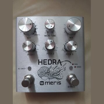 Stříbrný efekt pedál s kovovým povrchem a nápisy HEDRA a meris. Zařízení má pět ovládacích knoflíků s popisky KEY, MICRO TUNE, MIX, PITCH 1 a PITCH 2…