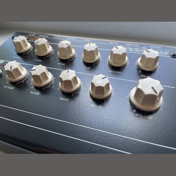 Černý elektronický přístroj s řadou bílých plastových oválových ovladačů. Na horní hraně jsou nápisy 12 VDC, OVERALL, GATE, SWITCH, AUDIO, MIDI IN, M…