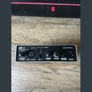 Stříbrné USB audio rozhraní s černými ovládacími prvky a konektory. Na zařízení jsou nápisy UR12, USB AUDIO INTERFACE 24bit/192kHz a logo steinberg.…