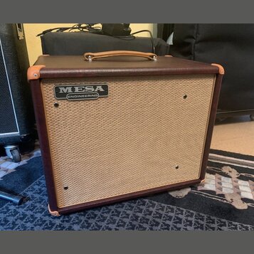 Kytarový kombo zesilovač v hnědém vinylovém potahu s koženou rukojetí a rohovými chrániči. Přední mřížka je v béžové barvě a nese stříbrno-černý ovál…