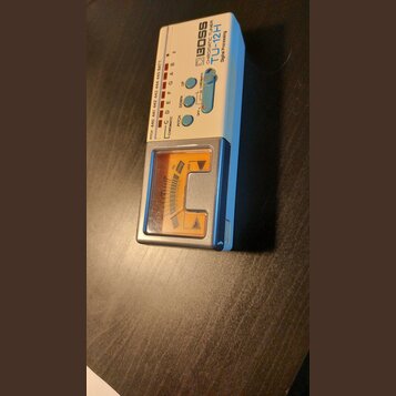 Bílý ladicí přístroj s modrým rámem a analogovým displejem. Na horním panelu jsou nápisy BOSS, CHROMATIC TUNER a TU-12H Digital Processing. Zařízení…