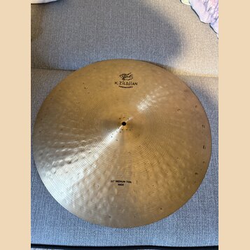 Zlatavý kovový činel s viditelným kovaným povrchem. Na horní části je černý nápis K.ZILDJIAN a pod ním menší text CONSTANTINO PLEI spolu s logem. Ve…