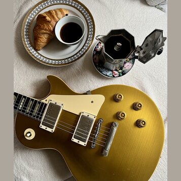 Zlatá elektrická kytara s tvarem singlecut, krémovým pickguardem a dvěma humbuckery. Na kytaru jsou vidět drobné škrábance a opotřebení povrchu. Vedl…