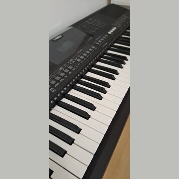 Černý digitální klavír s bílými a černými klávesami. V levé horní části je viditelné logo YAMAHA. Ovládací panel obsahuje řadu tlačítek s nápisy jako…